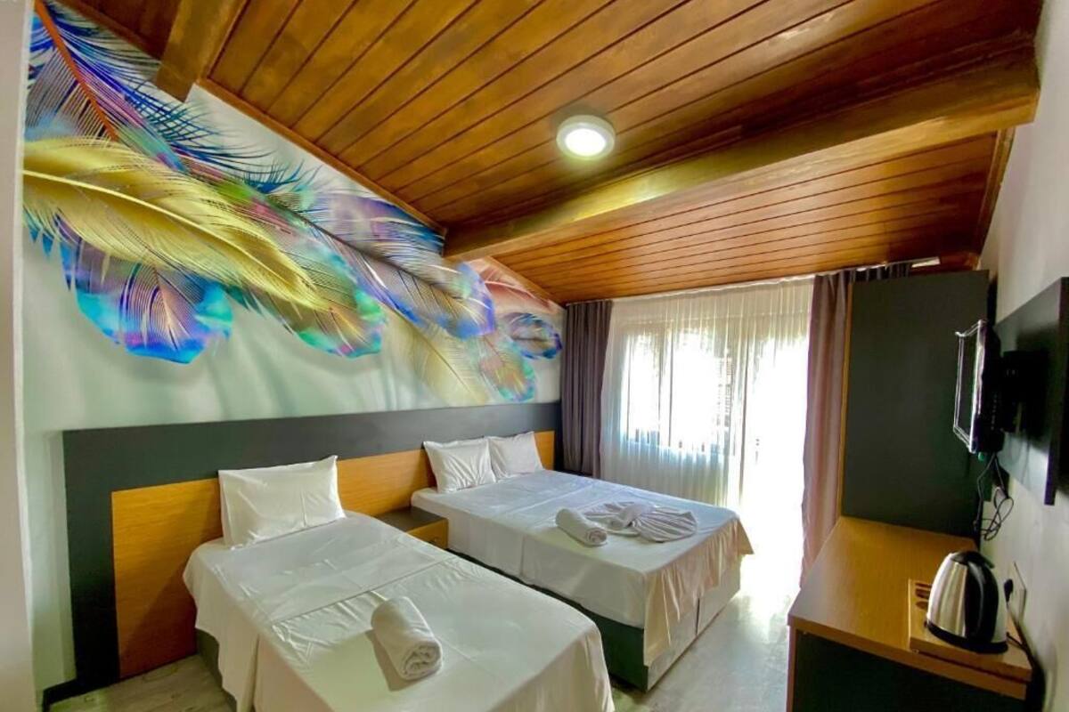 A hotel room with two beds, a wooden ceiling, a peacock feather mural, a television, and a kettle.
