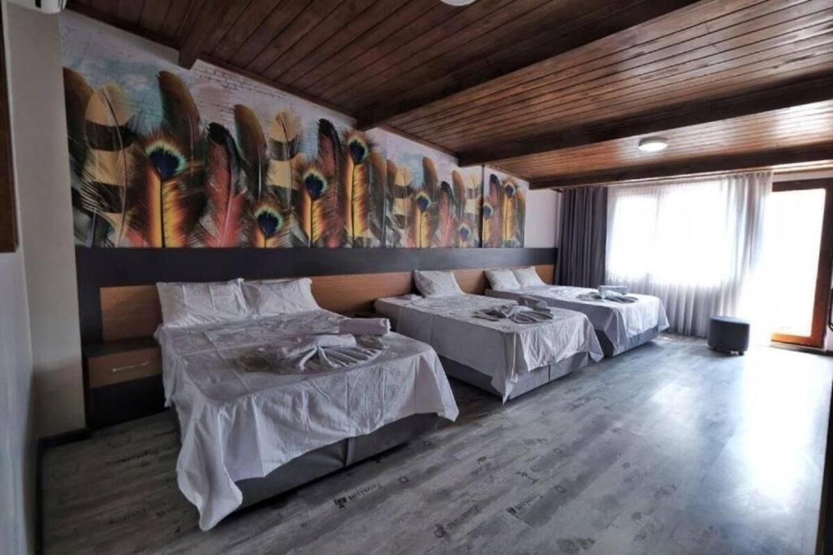 A hotel room with three single beds, a wooden ceiling, and a large peacock feather mural on the wall.