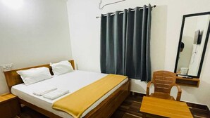A hotel room with a wooden bed, a small wooden table, a chair, a nightstand, and a mirror on the wall. - Murdeshwar Comforts (Murudeshwara)