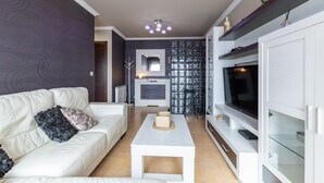 Uma sala de estar moderna com um sofá branco, uma mesa de centro e uma TV sobre um móvel.
