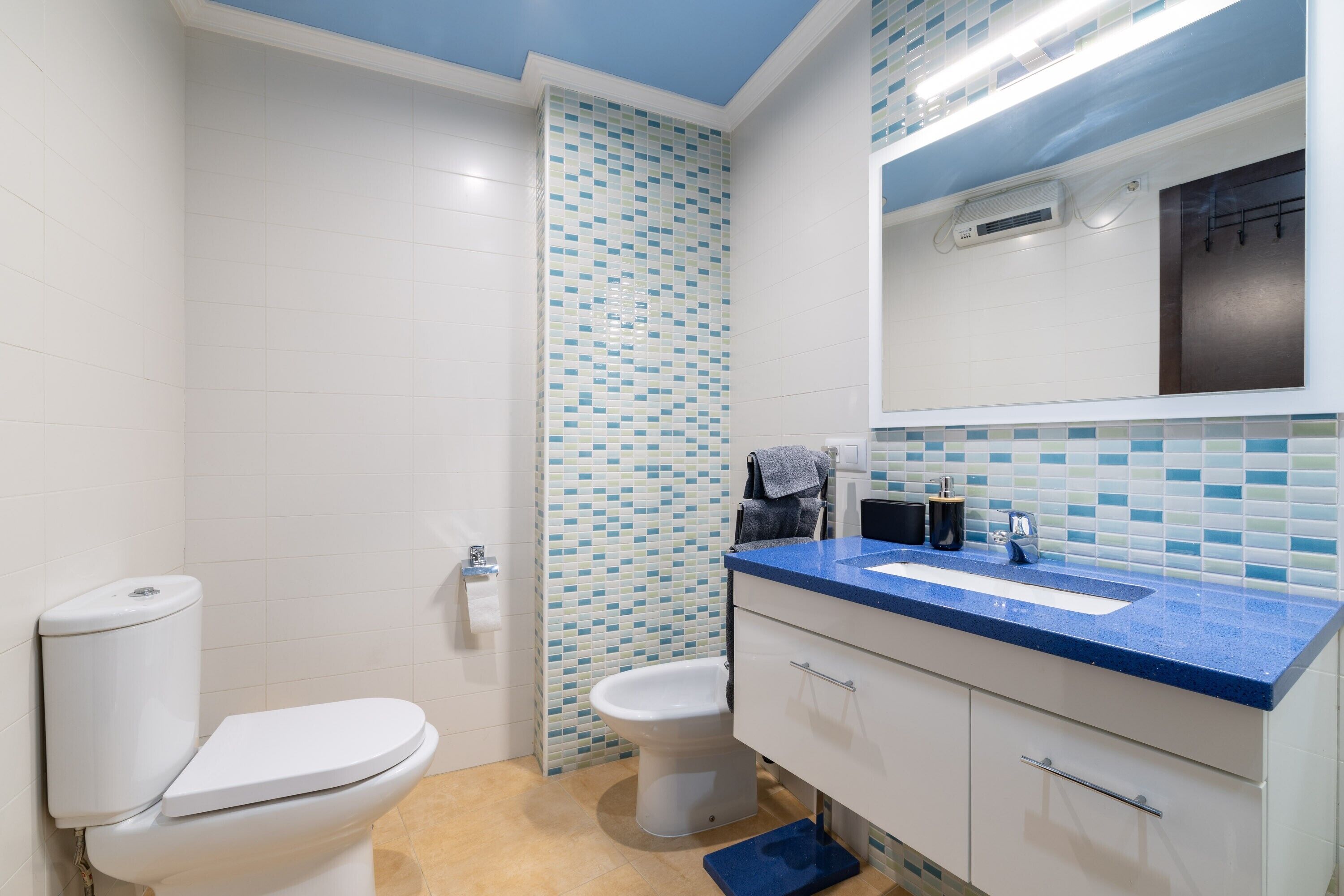 A bathroom with a toilet, bidet, sink, and mirror.