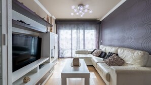 Uma sala de estar moderna com televisão de tela plana, sofá, mesa de centro e luminária decorativa.