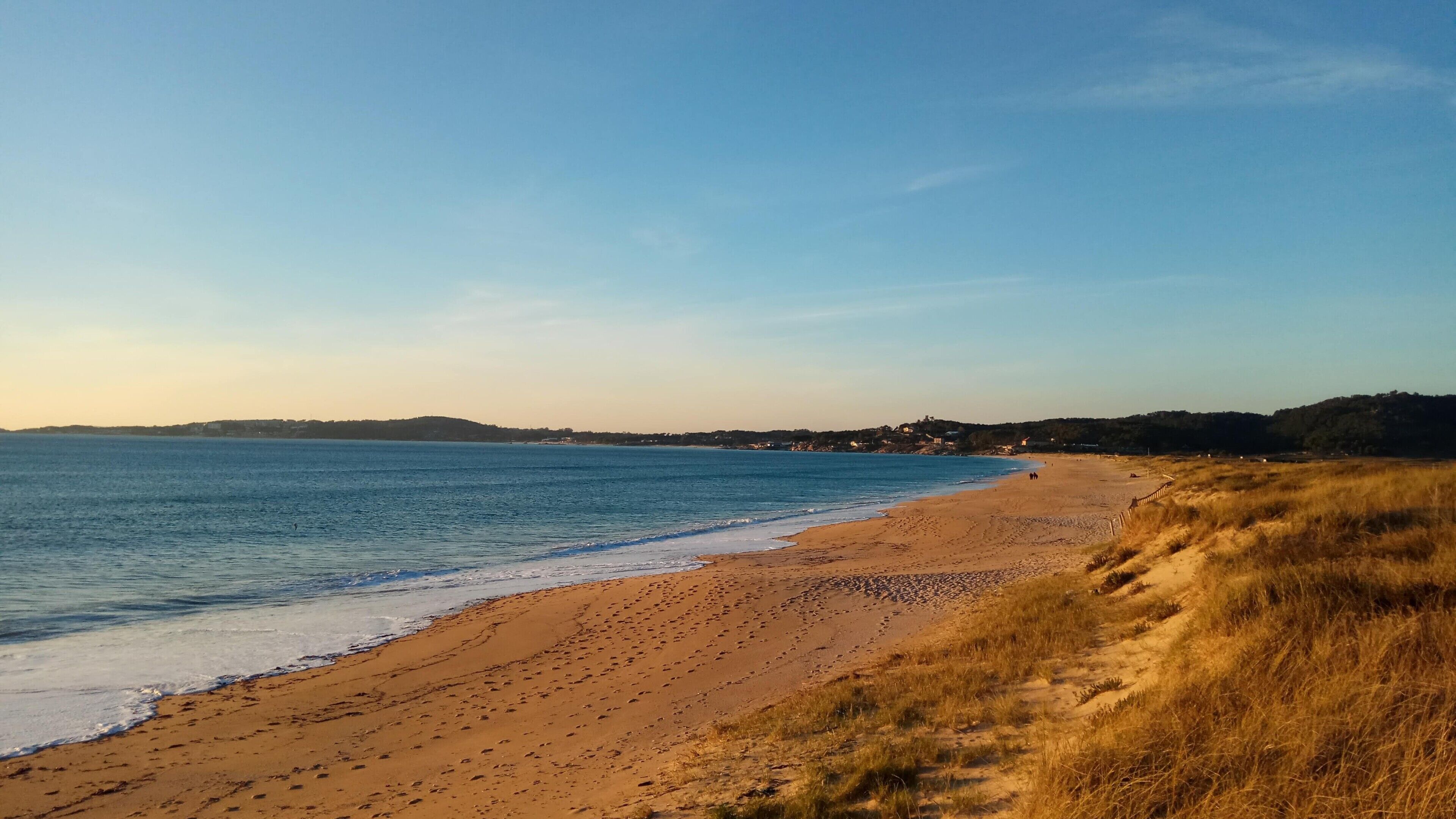 Una spiaggia con cielo sereno, spiaggia sabbiosa e colline all'orizzonte.