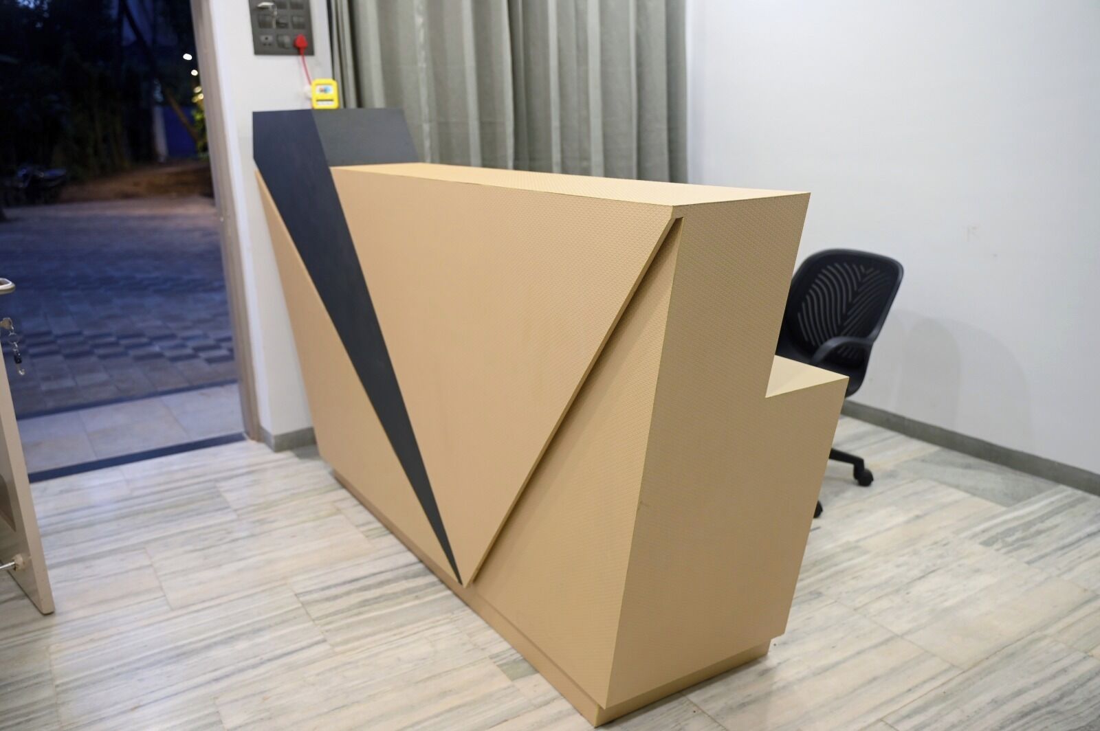 A room with a wooden reception desk, a black office chair, and a tiled floor.
