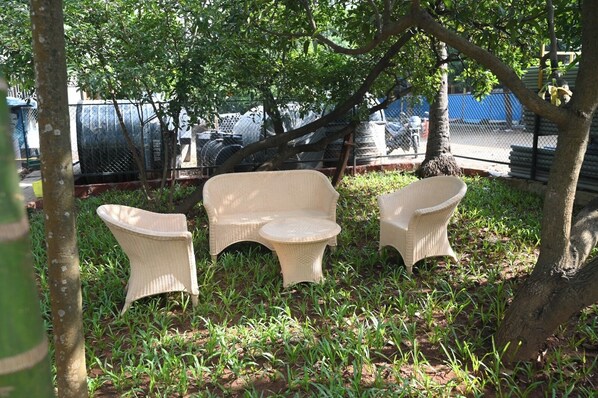 A garden area with three wicker chairs and a small table, surrounded by trees and grass. - Aqua Nova Resort (Alibag)