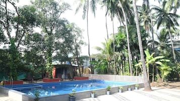 A swimming pool with a tiled deck, surrounded by palm trees and potted plants.