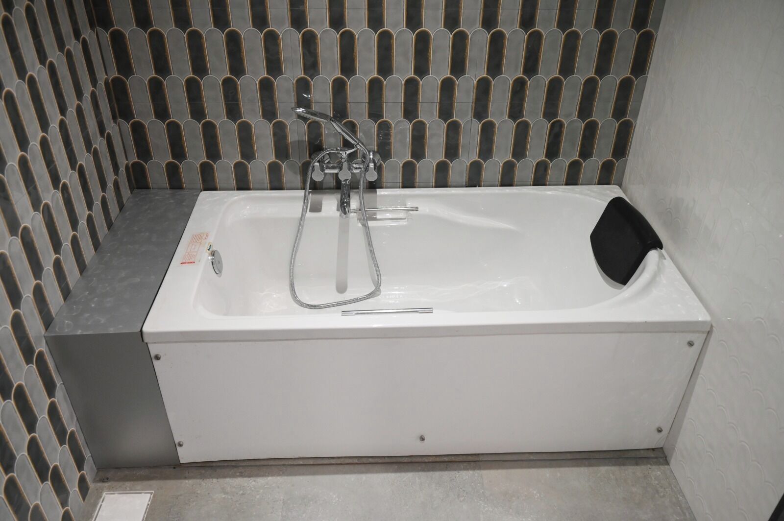 A white bathtub with a handheld showerhead and a black seat.