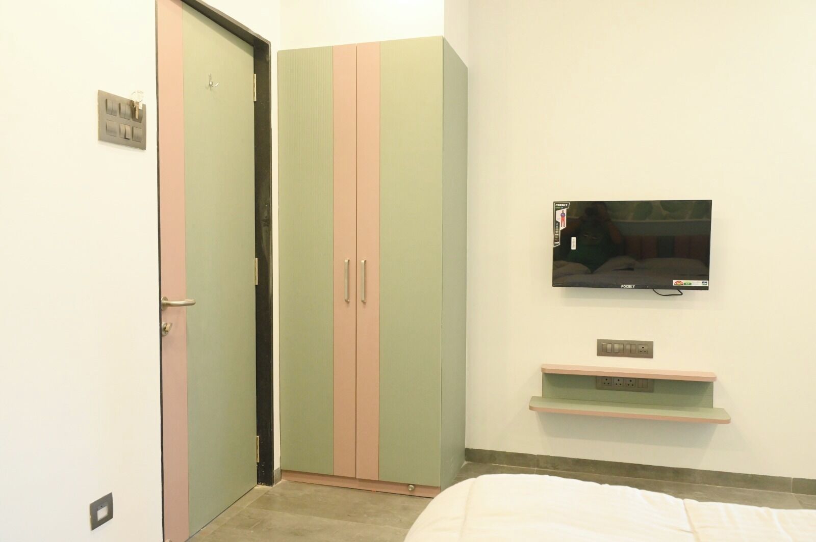 A bedroom with a bed, a TV mounted on the wall, and a wardrobe with two doors.