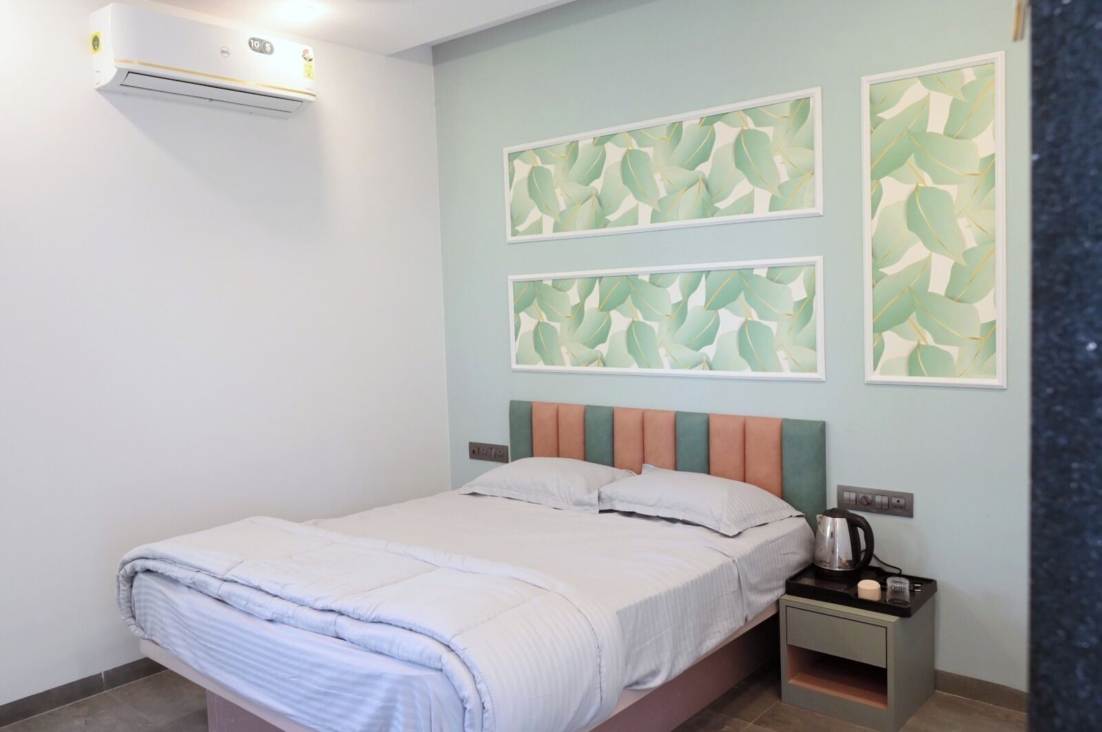 A bedroom with a bed, a nightstand, an air conditioner, and two wall-mounted artworks.