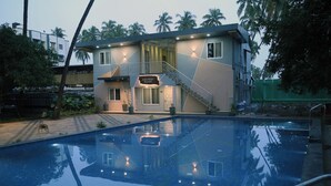En modern byggnad med en skylt som visar texten ”AQUA NOVA RESORT” intill en swimmingpool.