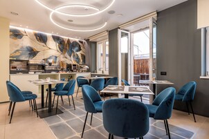 Un área de comedor moderna con sillas y mesas azules, una cocina al fondo y un gran mural abstracto en la pared.
