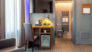 A hotel room with a desk, chair, mini-fridge, and a TV mounted on the wall. - Wega Hotel  (Verona)