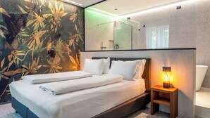 A modern hotel room with a large bed, a nightstand with a lamp, a bathroom with a mirror, and a wall with a floral pattern. - Wega Hotel  (Verona)