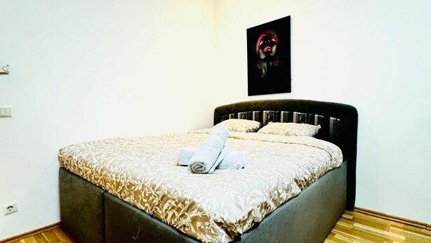 A bedroom with a bed, a wall-mounted picture, and a wooden floor.