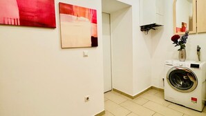A laundry room with a washing machine, a sink, and two abstract paintings on the wall.