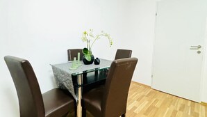 A dining area with a glass table, four brown chairs, a vase with flowers, and a white door.