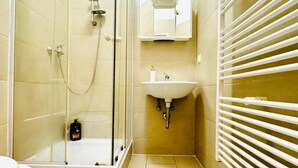 A bathroom with a glass shower enclosure, a sink with a mirror above, and a white towel rack.