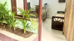 A room with a small garden area, a wooden chair, a table, and a cabinet. - Poonam Villas (New Delhi)