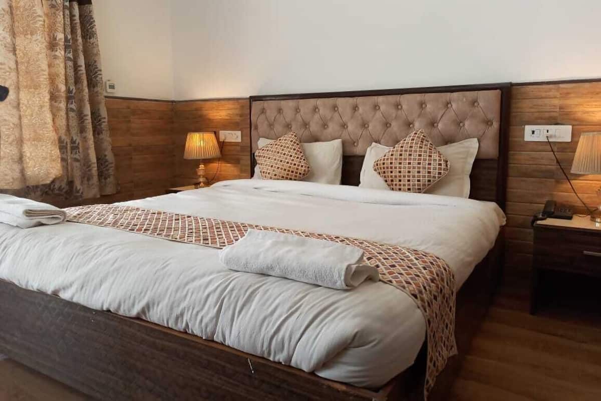 A neatly made bed with a patterned bedspread, two decorative pillows, a bedside lamp, and a wooden nightstand with a phone.