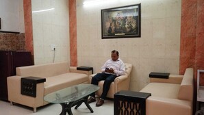 A man sitting on a beige sofa in a room with a glass coffee table, a framed picture on the wall, and a tiled floor. - Poonam Villas (New Delhi)