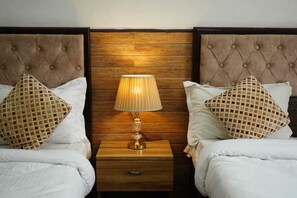 A hotel room with two beds, each with a tufted headboard, a wooden nightstand with a lamp, and patterned pillows.