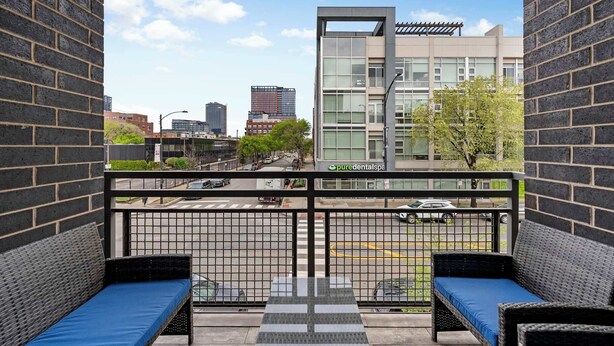 A balcony with wicker furniture, a view of a cityscape, and a building with a sign for 'puredentalspa'.
