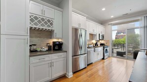 A modern kitchen with white cabinetry, stainless steel appliances, and a large window offering a view of the city.