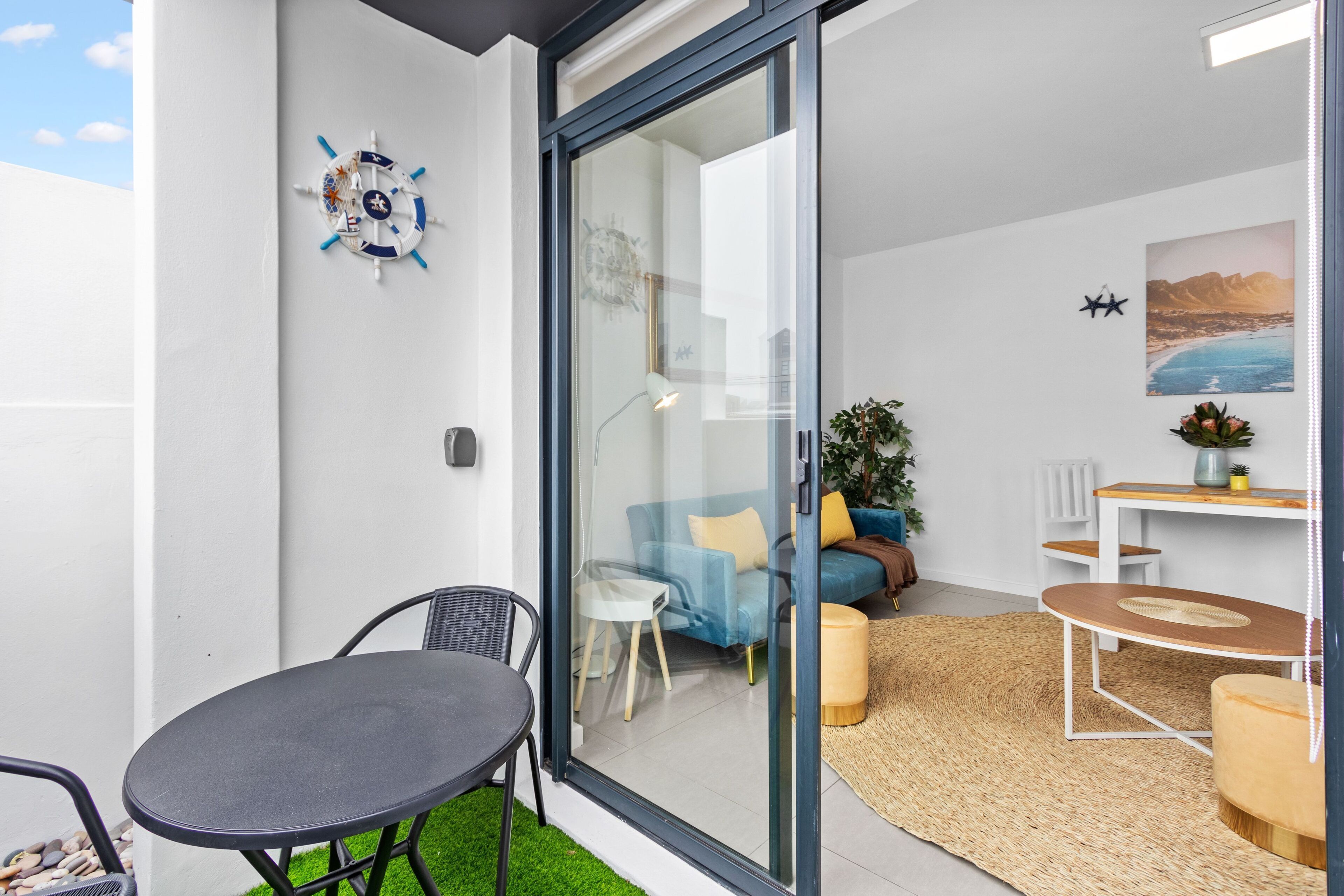 A modern living space with a glass door leading to a balcony, a blue sofa, a small table, and a potted plant.