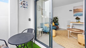 Un espace de vie moderne avec une porte vitrée donnant sur un balcon, un canapé bleu, une petite table et une plante en pot.
