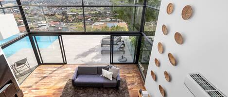 A modern living room with a large glass wall, a pool, and a view of a cityscape.