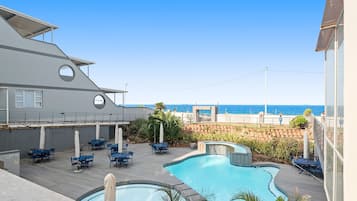 A pool area with lounge chairs and a view of the ocean.