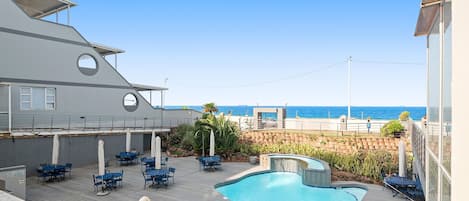 Área da piscina com espreguiçadeiras e vista para o oceano.