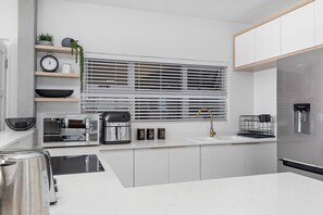 A modern kitchen with white cabinetry, a built-in microwave, a coffee maker, and a stainless steel refrigerator. - Perna Perna Coastal Escape (eMdloti)