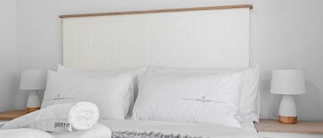 A neatly made bed with white bedding and a grey blanket, two bedside lamps, and a wooden headboard.