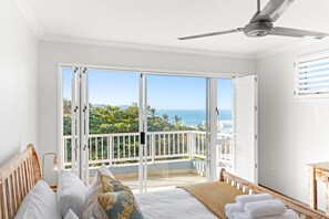 Ein Schlafzimmer mit einer großen Schiebeglaswand, die auf einen Balkon mit Meerblick führt.