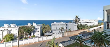 A coastal residential area with modern white buildings, a clear view of the sea, and a street with cars.