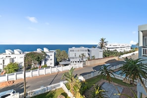 A coastal residential area with modern white buildings, a clear view of the sea, and a street with cars.