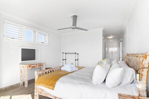 A bedroom with a bed, a ceiling fan, a TV, and a window with blinds. - San Marino 17 (Ballito)