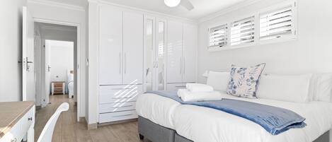 A bedroom with a bed, white wardrobe, ceiling fan, and a window with blinds.