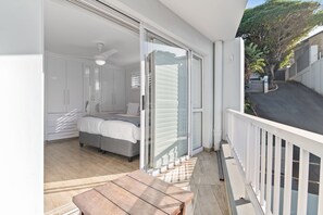 A balcony with a wooden table, a bed, and a sliding glass door leading to a bedroom. - San Marino 17 (Ballito)