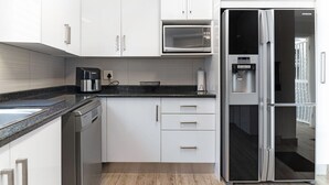 Eine moderne Küche mit weißen Schränken, einer eingebauten Mikrowelle, einer Kaffeemaschine und einem Kühlschrank.
