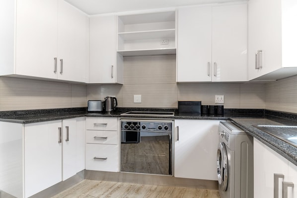 A modern kitchen with white cabinets, a built-in oven, a washing machine, and a coffee maker.