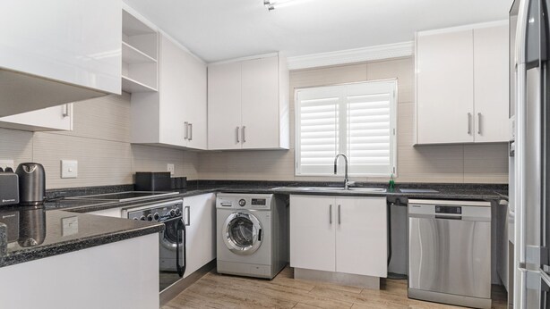 Une cuisine moderne avec des meubles blancs, un four encastré, un lave-linge et un lave-vaisselle.