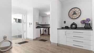 A modern kitchen with white cabinets, a built-in washing machine, and a decorative clock on the wall.