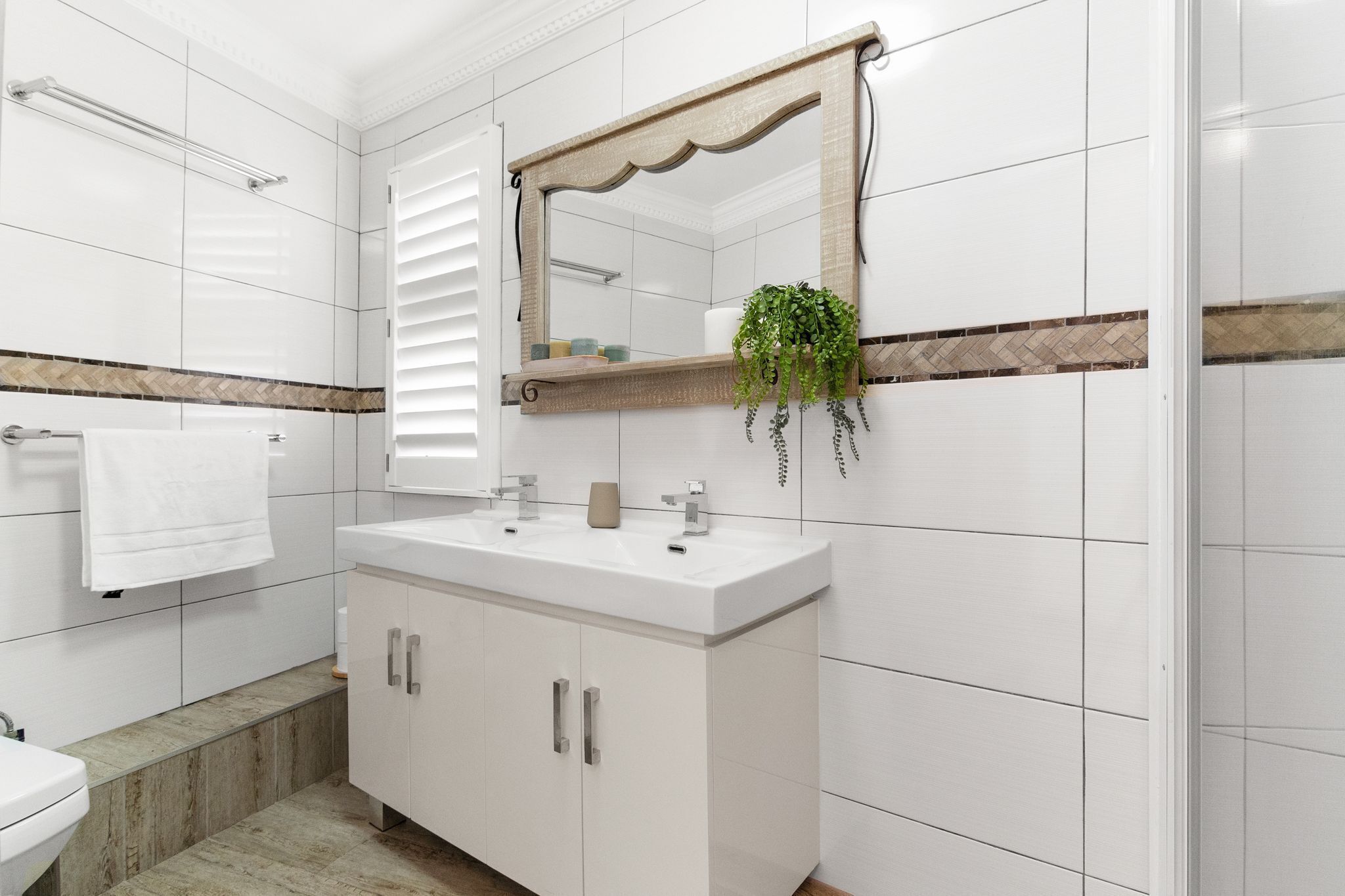 Une salle de bain moderne avec des carreaux blancs, un meuble-lavabo à deux vasques, un grand miroir et un porte-serviettes.