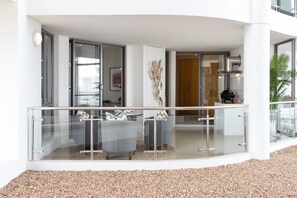 A modern outdoor seating area with glass railings, a stone floor, and a view into the building. - Hibernian Towers 503 (Cape Town)