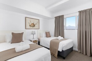 A hotel room with two beds, a bedside table with a lamp, a framed picture on the wall, and a window with curtains. - Odeon Towers 1102 (Cape Town)