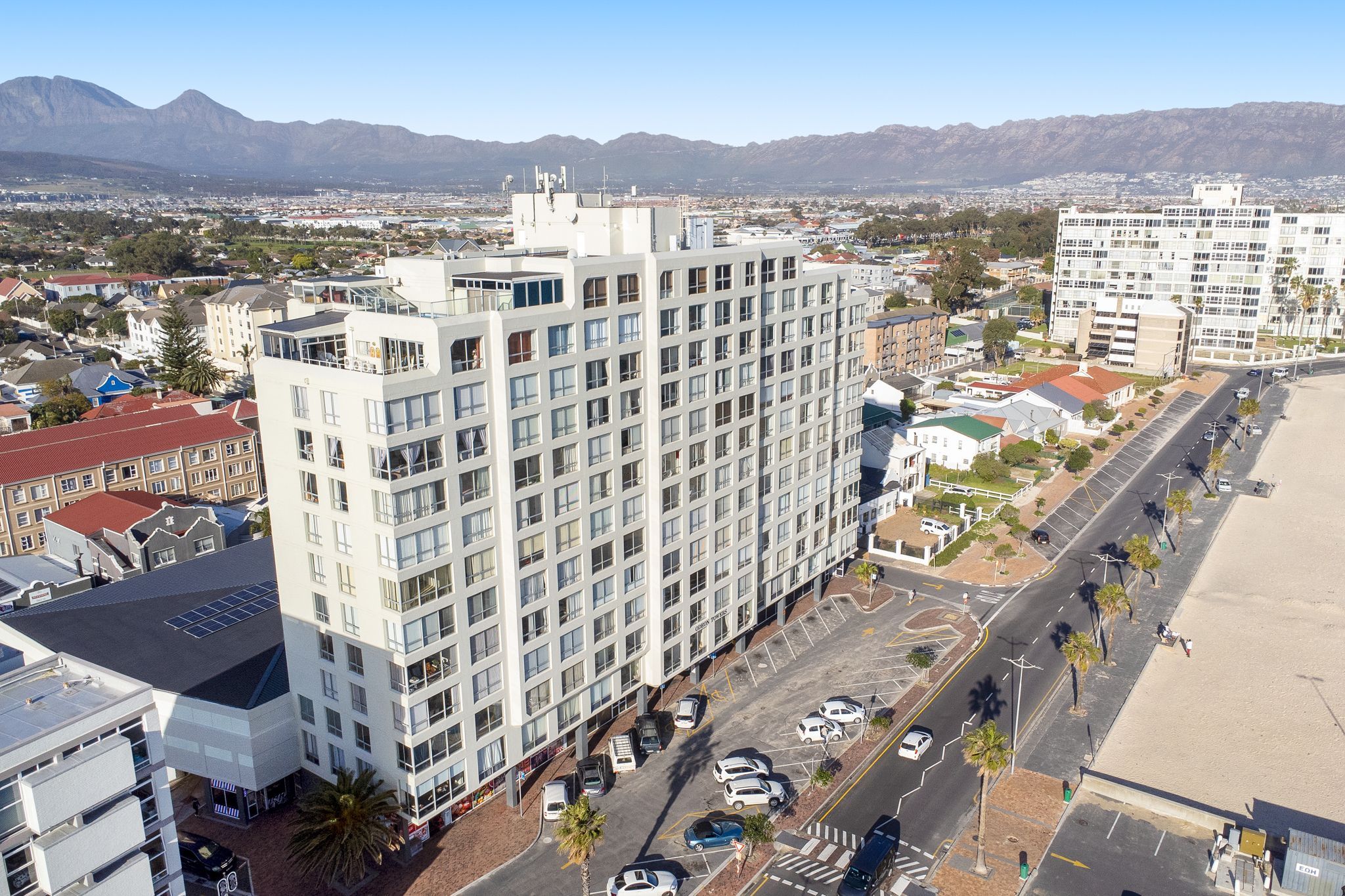 A high-rise hotel with multiple floors, a parking lot, and a view of the city and mountains in the background.