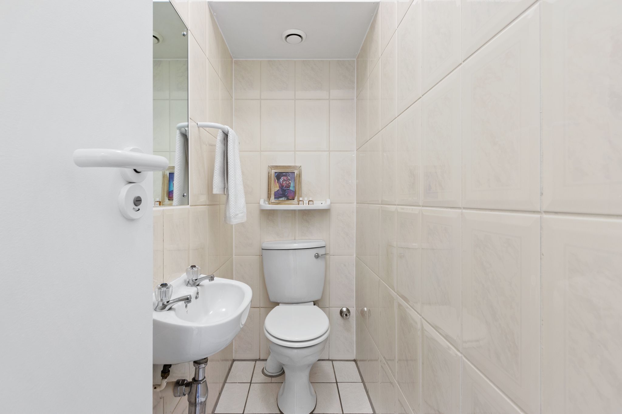 A bathroom with a white sink, toilet, and a framed picture on the wall.