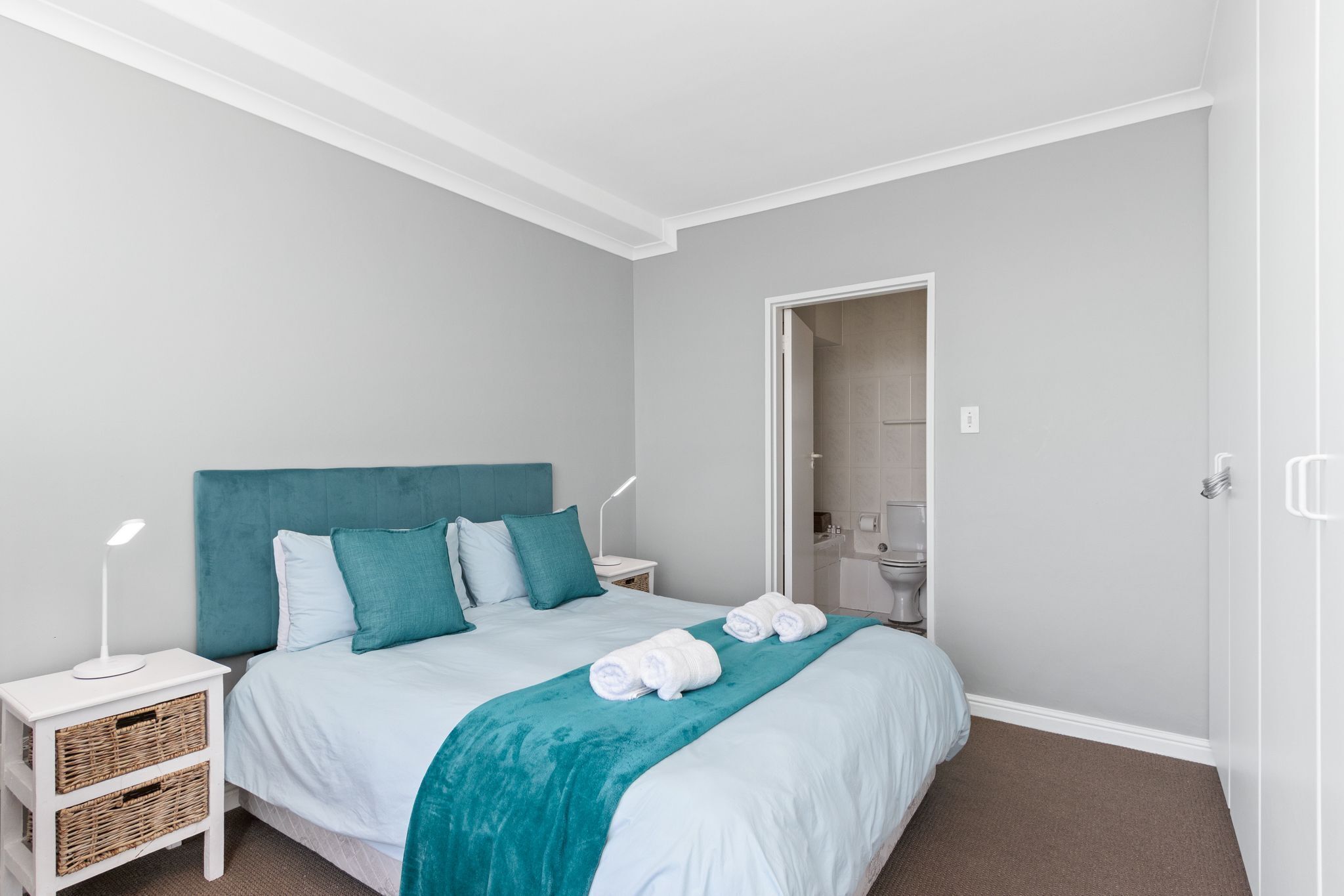 A neatly arranged bedroom with a bed, bedside tables, and a bathroom visible through an open door.